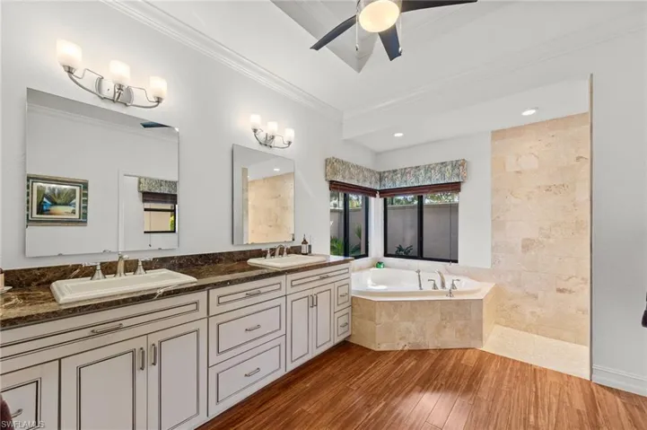 Full bath featuring double vanity, a bath, dark wood-style flooring, a ceiling fan, and crown molding