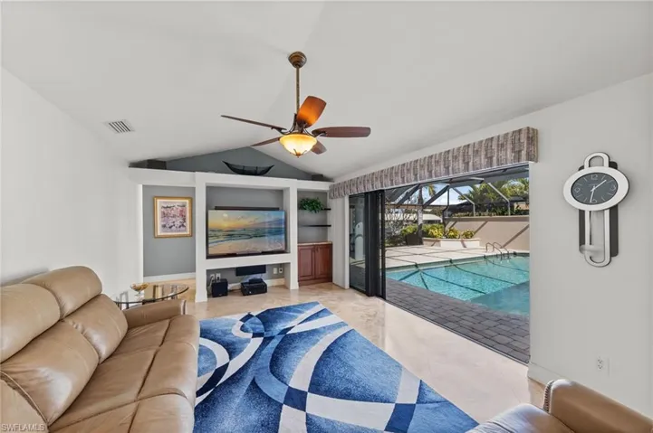 Living room with a sunroom, vaulted ceiling, a ceiling fan, and built in shelves