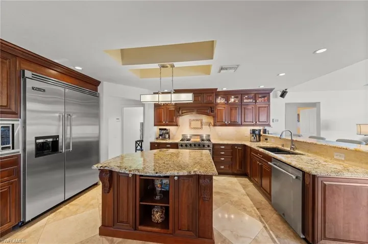 Kitchen featuring a peninsula, open shelves, built in appliances, a raised ceiling, and light stone counters