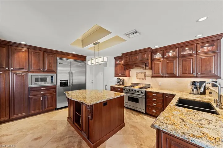 Kitchen with built in appliances, a kitchen island, light stone countertops, and light tile patterned flooring