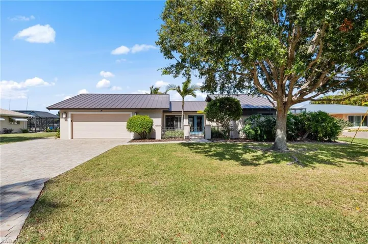 Ranch-style house featuring decorative driveway, a front yard, a metal roof, stucco siding, and an attached garage