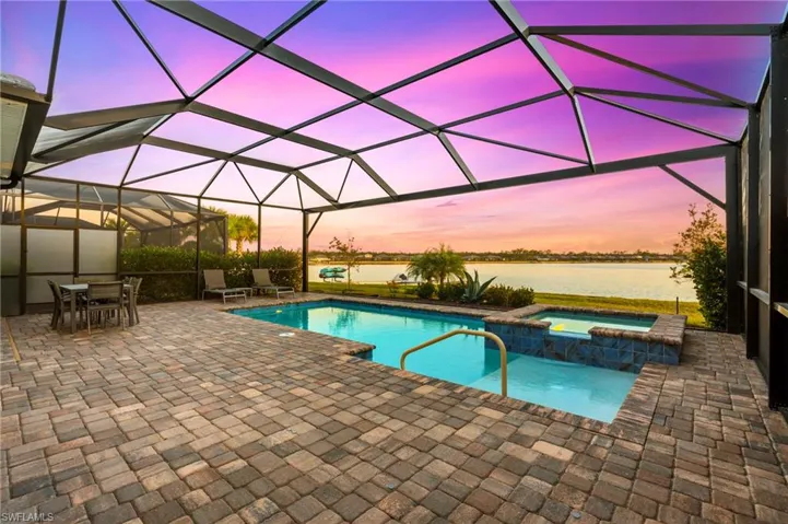 Pool at dusk featuring a lanai, a patio area, an in ground hot tub, and a water view