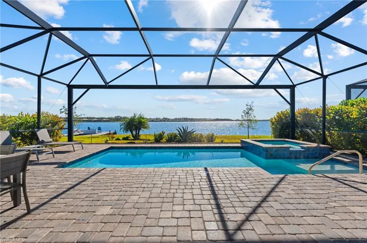 View of pool with glass enclosure, an in ground hot tub, a water view, and a patio