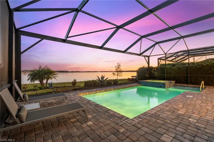 Pool at dusk with an in ground hot tub, a water view, a patio area, and a lanai