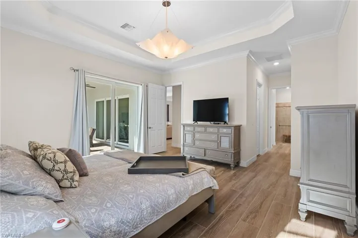 Bedroom with access to outside, a tray ceiling, light hardwood / wood-style flooring, and ornamental molding