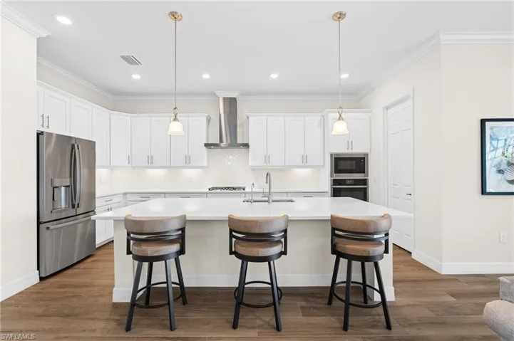 Kitchen featuring a center island with sink, wall chimney exhaust hood, white cabinetry, and appliances with stainless steel finishes