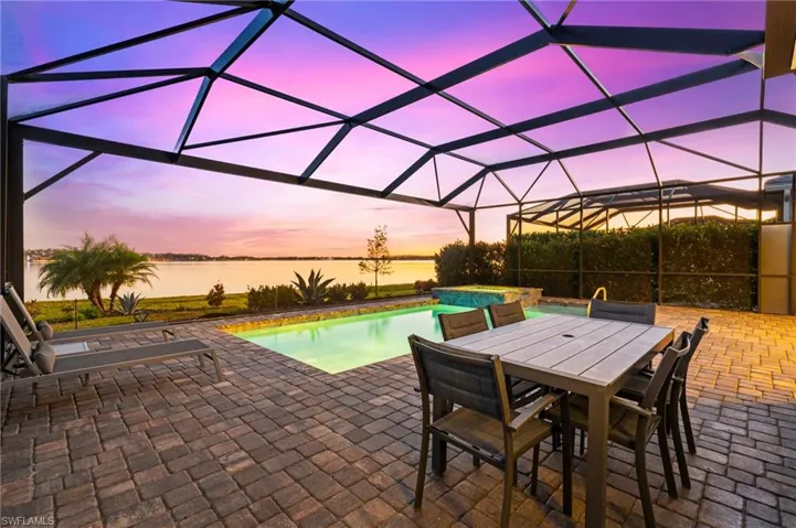 Pool at dusk with glass enclosure, an in ground hot tub, a water view, and a patio