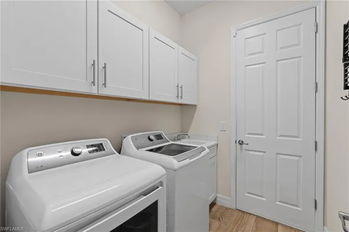 Laundry room with separate washer and dryer, light hardwood / wood-style flooring, and cabinets