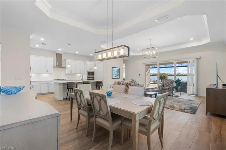 Dining space featuring sink, a raised ceiling, light hardwood / wood-style flooring, a notable chandelier, and crown molding