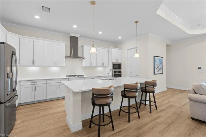 Kitchen with appliances with stainless steel finishes, white cabinetry, hanging light fixtures, and wall chimney exhaust hood