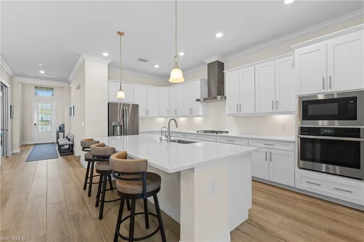 Kitchen featuring wall chimney range hood, stainless steel appliances, white cabinets, and sink