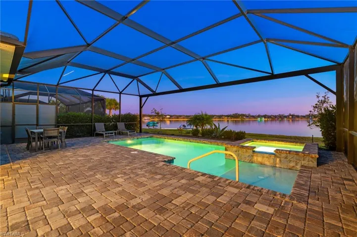 Pool at dusk with an in ground hot tub, a patio, a water view, and a lanai