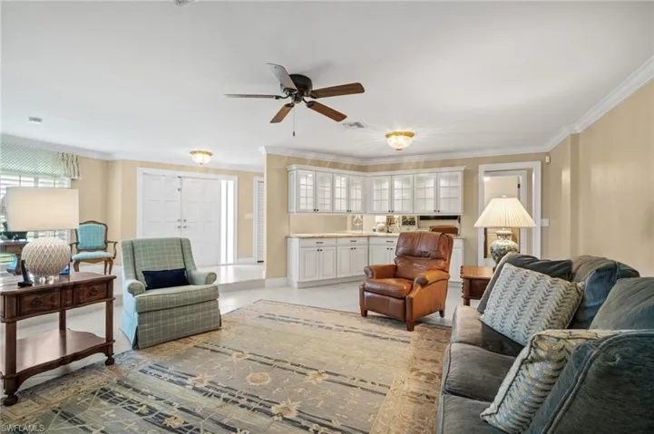 Living area with light tile patterned floors, visible vents, baseboards, ceiling fan, and ornamental molding