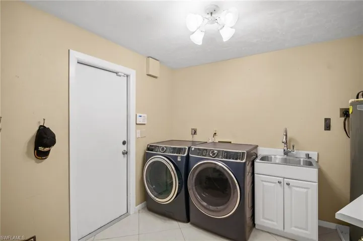 Washroom with light tile patterned floors, baseboards, washing machine and clothes dryer, cabinet space, and a sink