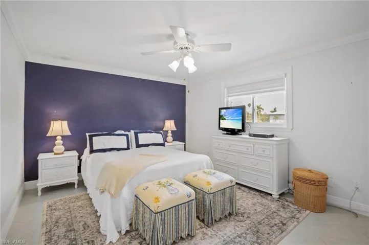 Bedroom featuring an accent wall, ceiling fan, baseboards, ornamental molding, and light tile patterned floors