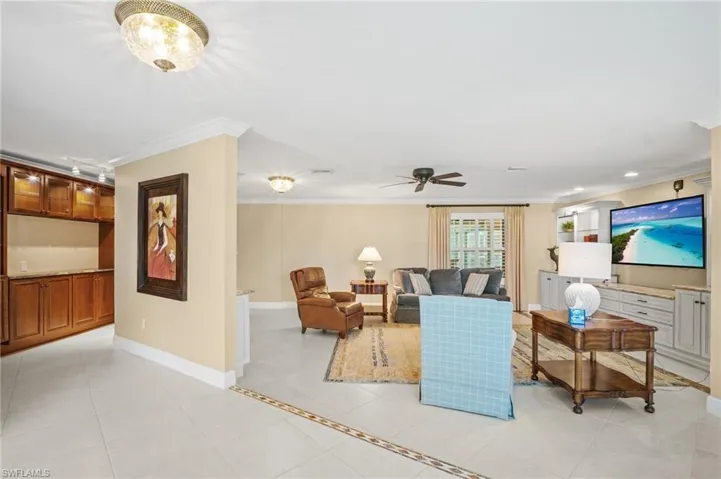 Living room featuring crown molding, light tile patterned flooring, a ceiling fan, and baseboards