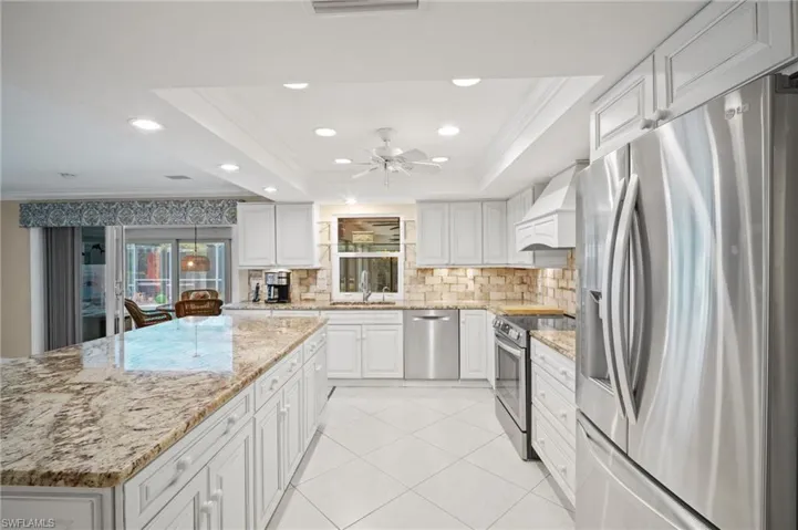 Kitchen featuring premium range hood, a sink, ornamental molding, stainless steel appliances, and a raised ceiling