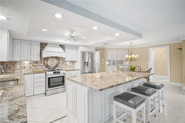 Kitchen with custom range hood, a sink, stainless steel appliances, crown molding, and a raised ceiling