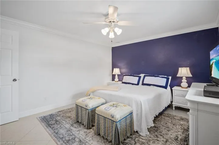 Bedroom featuring baseboards, ceiling fan, an accent wall, crown molding, and tile patterned floors