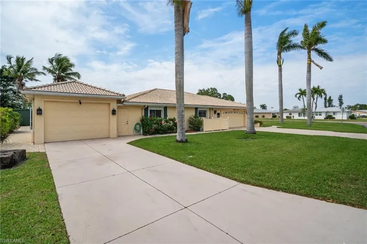 View of front of house featuring stucco siding, driveway, a tile roof, a front yard, and an attached garage