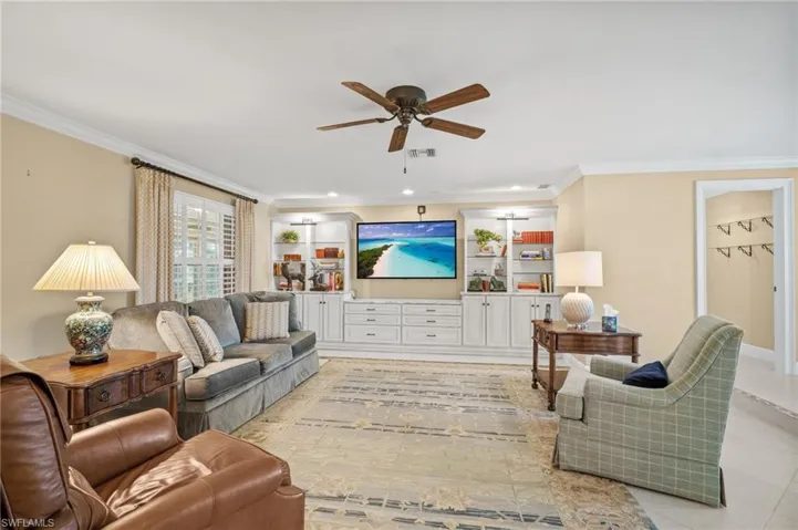 Living room with light tile patterned flooring, visible vents, a ceiling fan, and ornamental molding