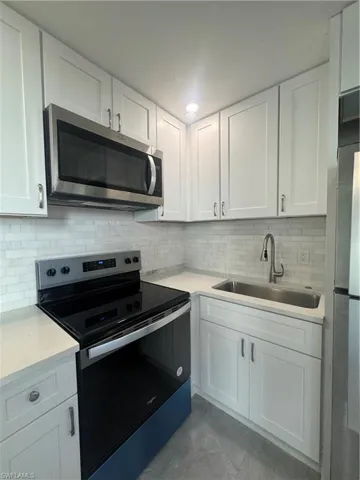 Kitchen featuring stainless steel stove, white cabinets, backsplash, and light stone countertops