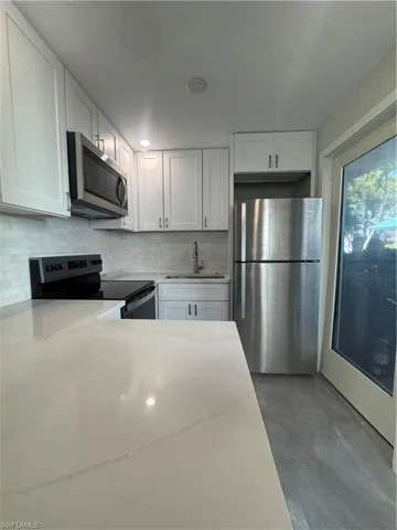 Kitchen with white cabinets, stainless steel refrigerator, range, and light stone counters