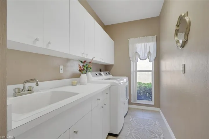 Laundry area featuring separate washer and dryer, light tile patterned flooring, and cabinet space