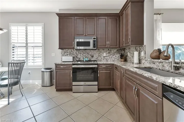 Kitchen with sink, decorative backsplash, light tile patterned floors, appliances with stainless steel finishes, and dark brown cabinets