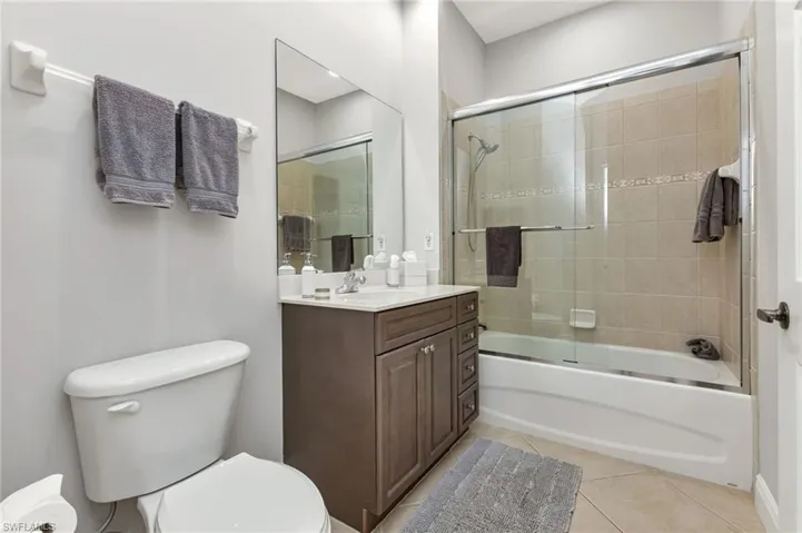 Full bathroom with toilet, tile patterned flooring, vanity, and combined bath / shower with glass door