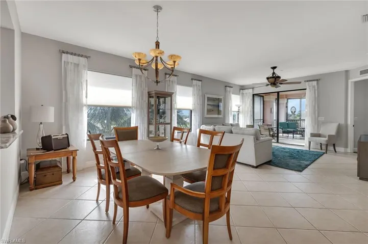 Dining area featuring light tile patterned floors, ceiling fan with notable chandelier, and a wealth of natural light