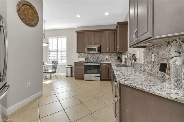 Kitchen featuring sink, hanging light fixtures, light tile patterned floors, appliances with stainless steel finishes, and dark brown cabinets