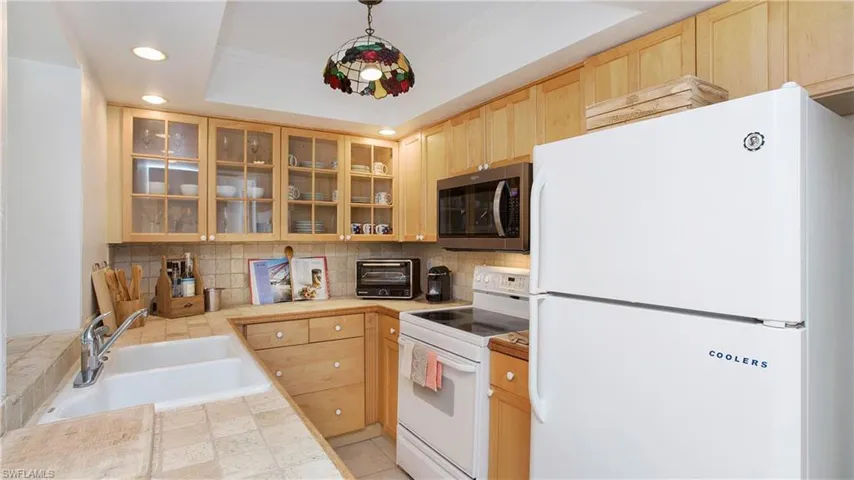 Kitchen with light brown cabinets, pendant lighting, a raised ceiling, sink, and white appliances