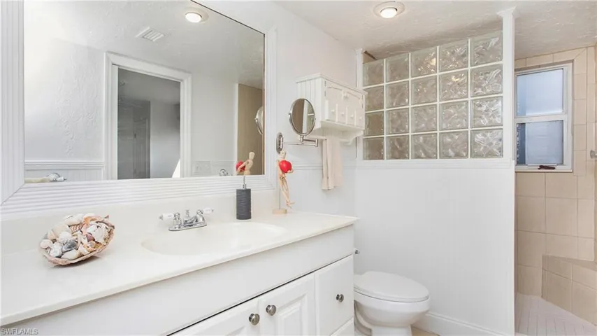 Bathroom featuring a textured ceiling, a tile shower, vanity, and toilet