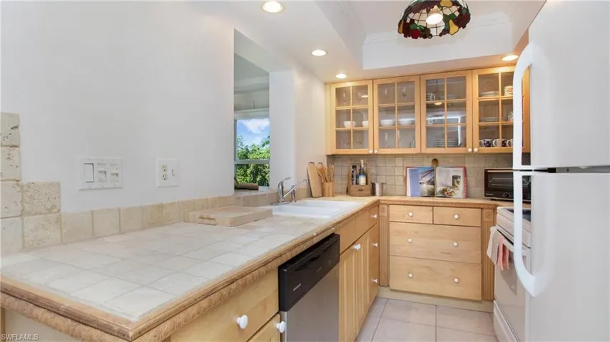 Kitchen with tile counters, sink, white appliances, backsplash, and ornamental molding