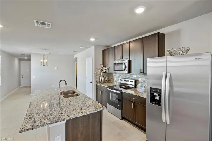 Kitchen featuring stainless steel appliances, a kitchen island with sink, sink, light tile floors, and pendant lighting