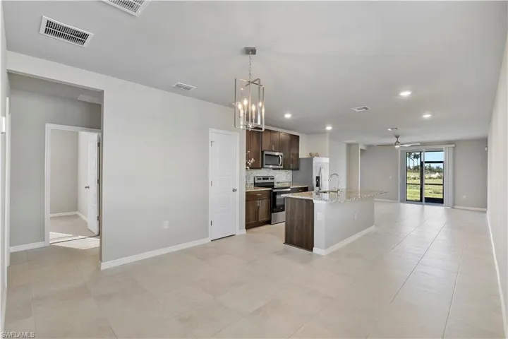 Kitchen featuring a center island with sink, decorative light fixtures, backsplash, light tile floors, and appliances with stainless steel finishes