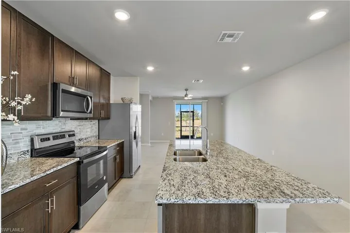 Kitchen featuring ceiling fan, an island with sink, light tile flooring, sink, and appliances with stainless steel finishes