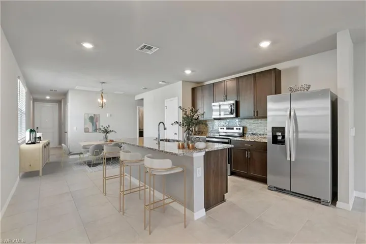 Kitchen featuring light stone counters, sink, an island with sink, decorative backsplash, and appliances with stainless steel finishes