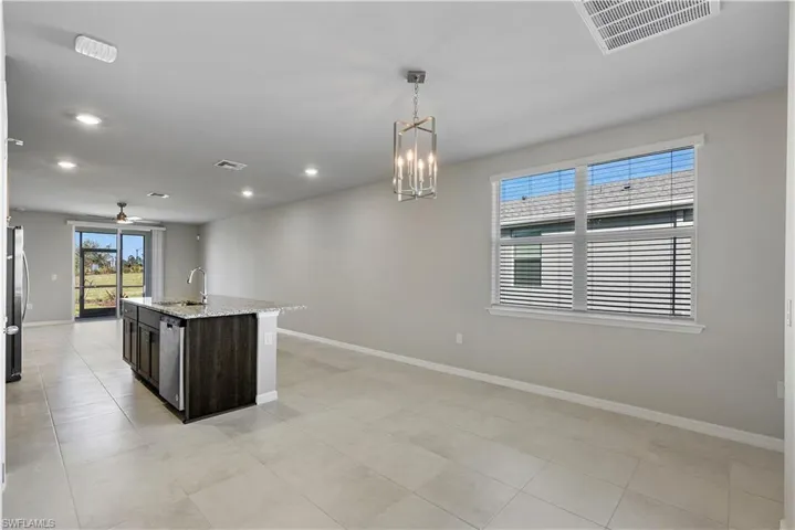 Kitchen featuring a center island with sink, decorative light fixtures, ceiling fan with notable chandelier, light tile floors, and sink