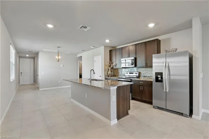 Kitchen with a center island with sink, appliances with stainless steel finishes, sink, tasteful backsplash, and light tile floors