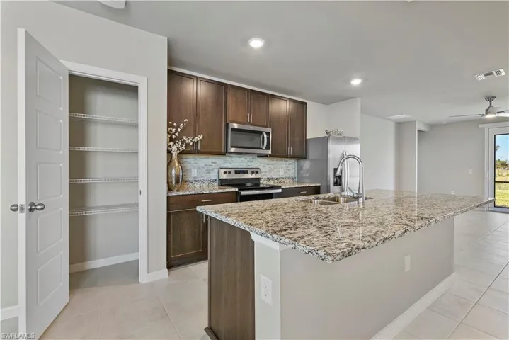 Kitchen with appliances with stainless steel finishes, a kitchen island with sink, tasteful backsplash, ceiling fan, and light tile floors