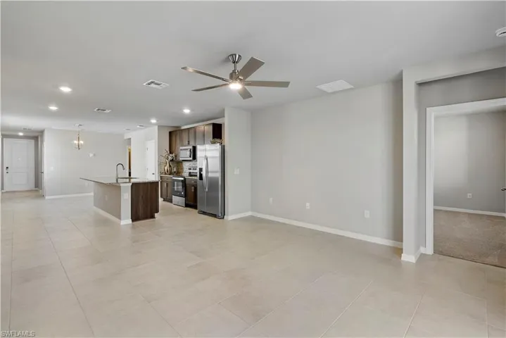 Kitchen with stainless steel appliances, a center island with sink, ceiling fan, and light tile flooring