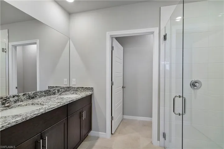Bathroom featuring tile floors, a shower with door, vanity with extensive cabinet space, and double sink