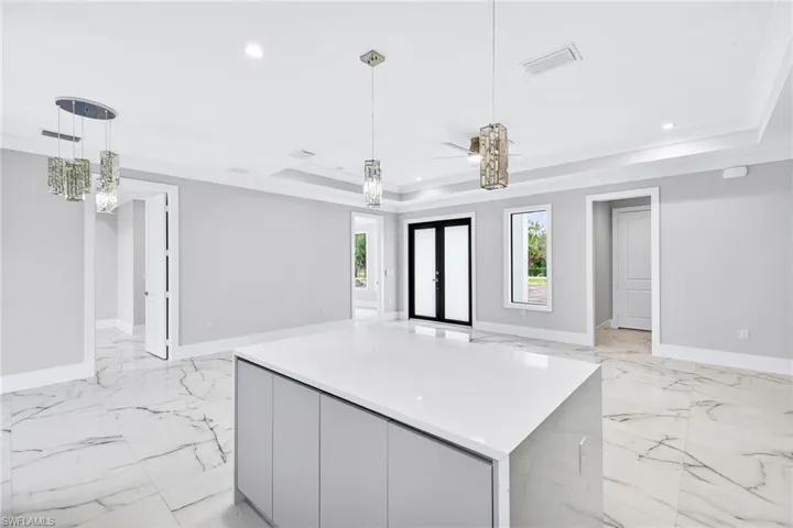 Kitchen featuring hanging light fixtures, a kitchen island, modern cabinets, light stone countertops, and ornamental molding