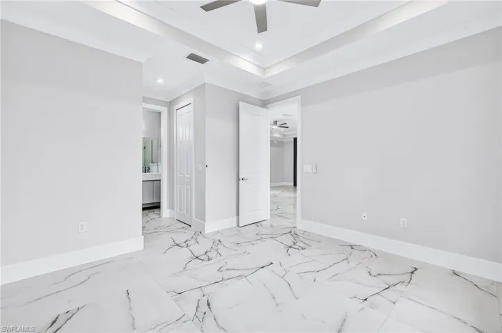 Unfurnished bedroom featuring ensuite bathroom, recessed lighting, ornamental molding, a raised ceiling, and ceiling fan