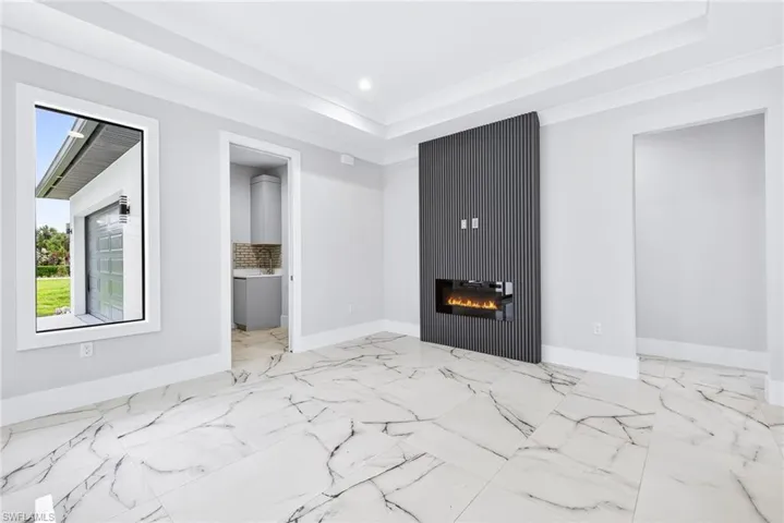 Unfurnished living room with a tray ceiling, a glass covered fireplace, light marble finish floors, and recessed lighting