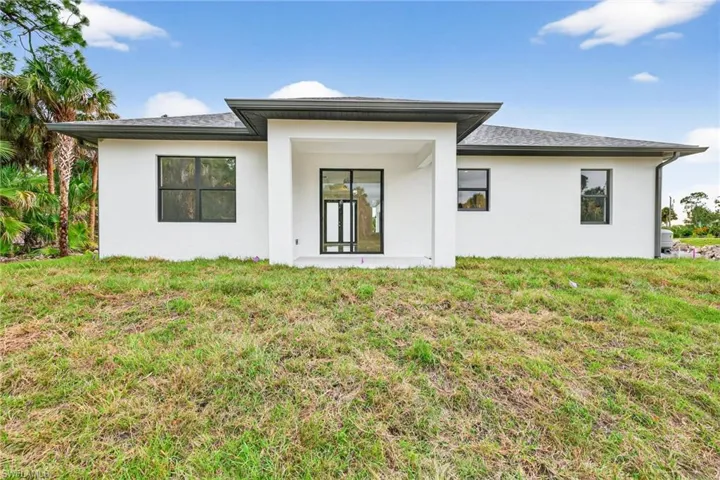 Back of property with stucco siding, a lawn, and a patio area