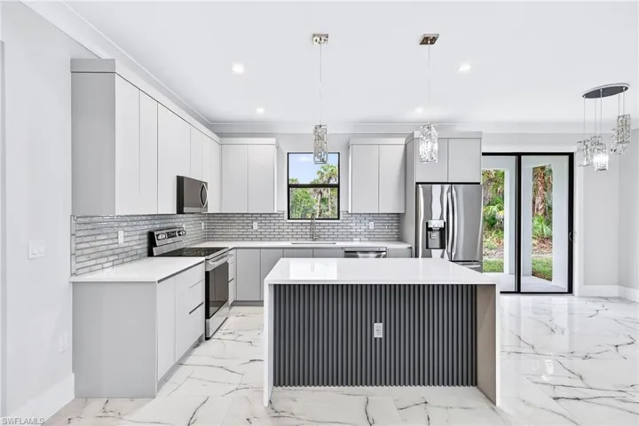 Kitchen with modern cabinets, pendant lighting, stainless steel appliances, and light stone counters