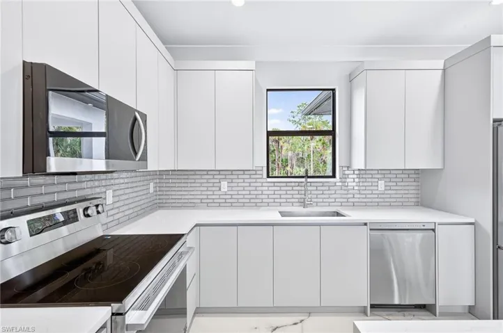 Kitchen with stainless steel appliances, modern cabinets, white cabinetry, light stone countertops, and recessed lighting